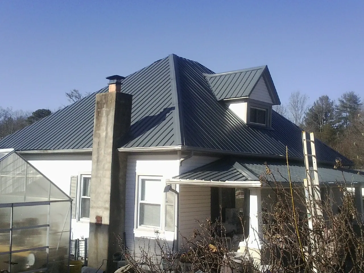 Dark blue standing seam metal roof on a white farmhouse with dormer — Slate & Tile Roof Repair by Roofing Brothers in Blossvale