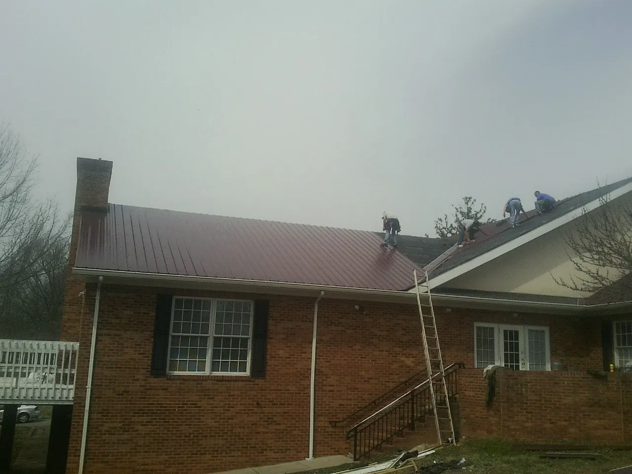 Crew setting red metal roofing panels on a brick home in Blossvale