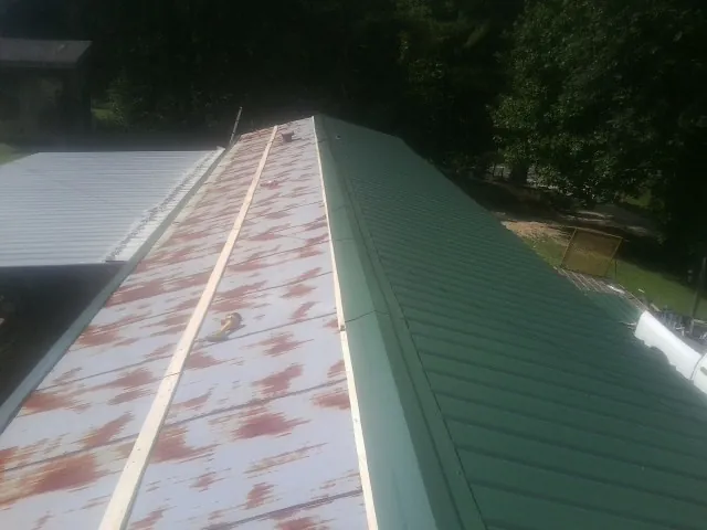 Old rusted panels beside newly installed green metal roofing — Wind Damage Roof Repair by Roofing Brothers in Blossvale