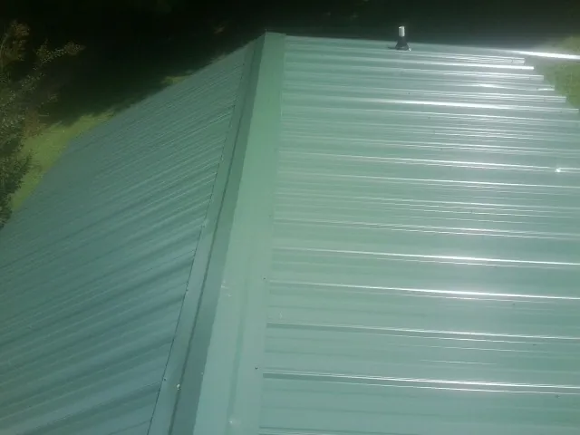 New green metal panels meeting at the ridge of a roof — Flat Roof Repair work by our crew in Blossvale