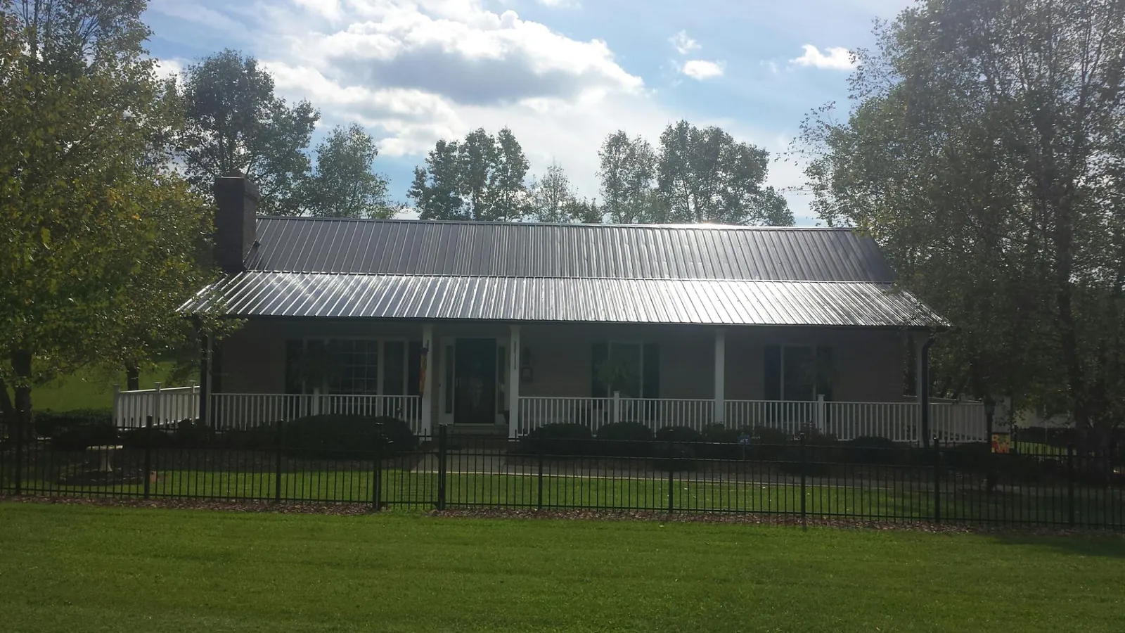 Gray metal roof on a brick ranch with a full width front porch — Gutter Guard Installation work by our crew in Blossvale