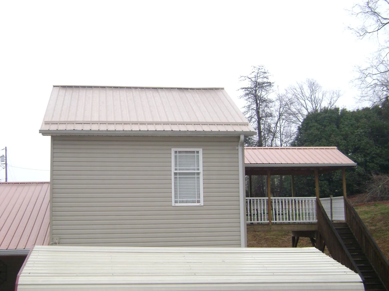 Tan metal roofs on a two story addition and attached porch, from a Roof Replacement job in Blossvale